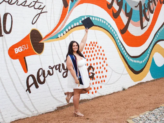 BGSU grad poses with grad cap in front of the BGSU mural