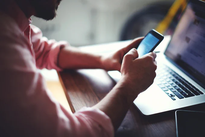 A picture of a man holding a phone in front of a laptop.