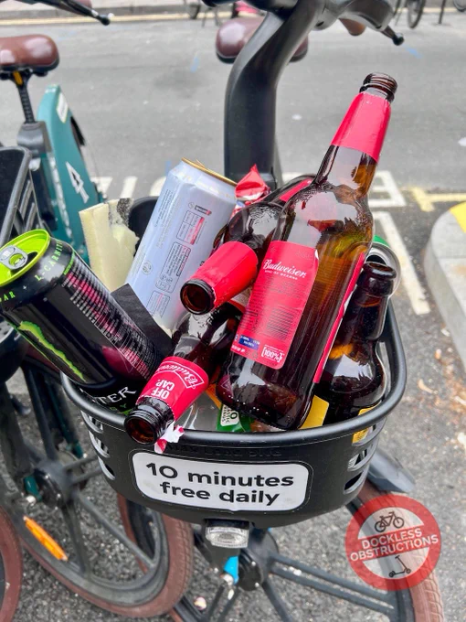 Photo of a dockless cycle hire ebike front basket full of empty beer bottles and cans - used as a street bin.