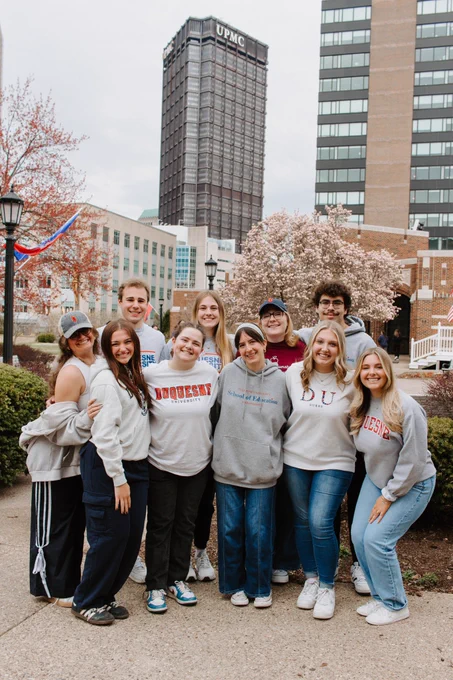 Group of students in a group smiling together and wearing Duquesne apparel.