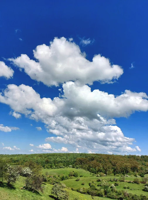 A photo of the rolling Kišelez meadow with beautiful clouds over green hills.