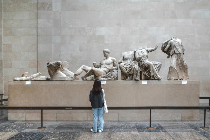 Visitor observing the Elgin Marbles, a collection of classical Greek marble sculptures from the Parthenon, displayed in a museum gallery.