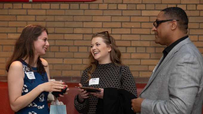 Three people standing together talking and laughing