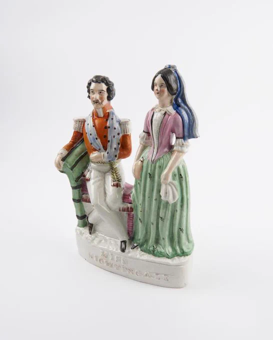 Pottery figure showing a man with his arm in a sling and a woman in a green and pink dress.