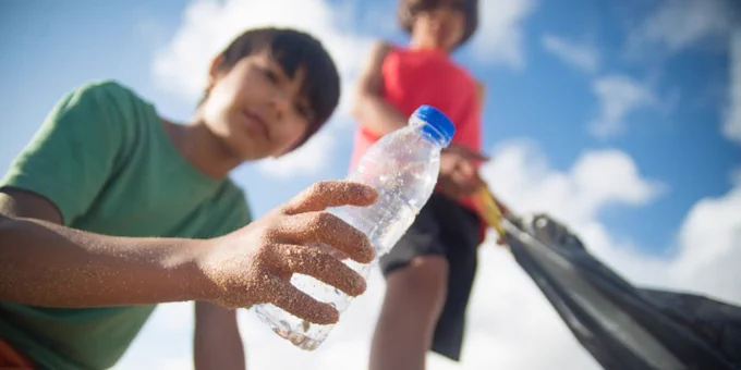 Children participating in a beach cleanup, collecting plastic bottles and trash on a sunny day.