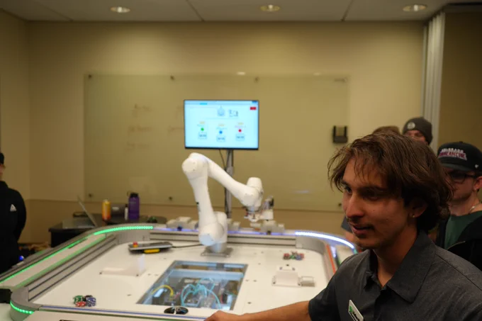 A student stands in front of a robotic arm that deals cards.