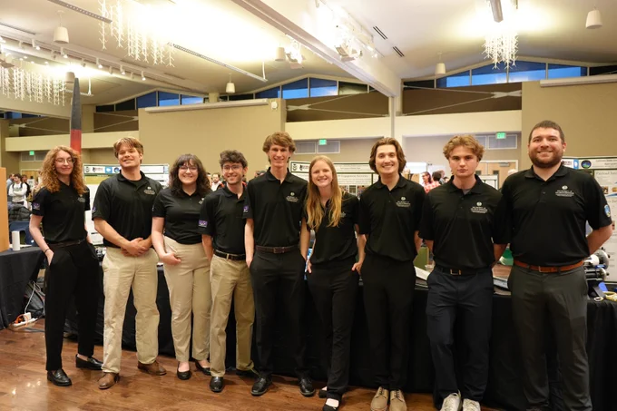 A group of students pose in front of a rocket.