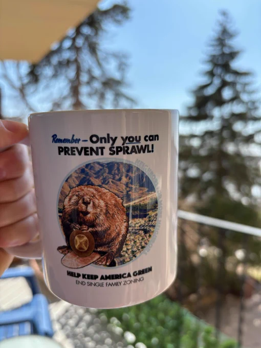 mug being held outside. Mug reads "Remember - only YOU can prevent sprawl! Help keep america green. End single family zoning." With a picture of a beaver holding a park ranger hat