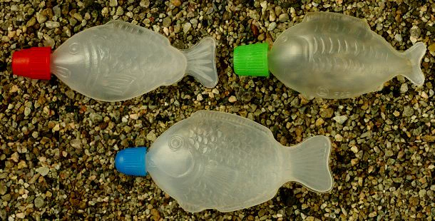 Three differently fish-shaped little soy sauce bottles on gravel. 