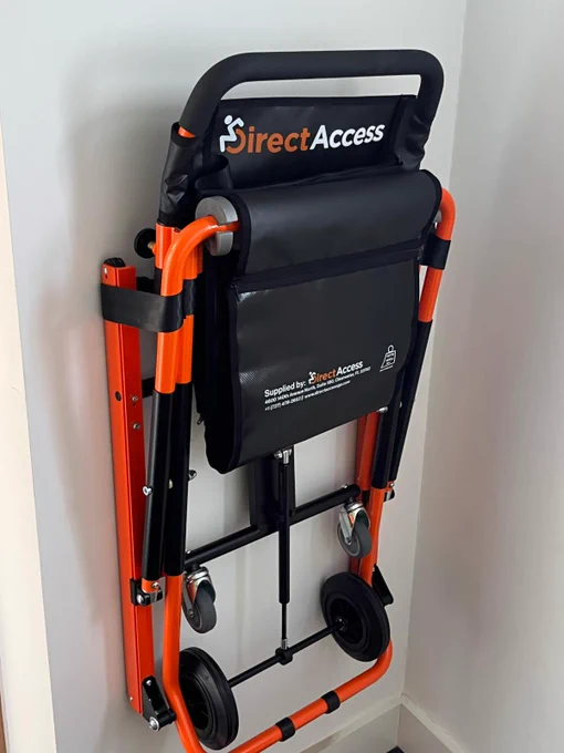 An orange Direct Access evacuation chair being held in place on a wall in a hallway.