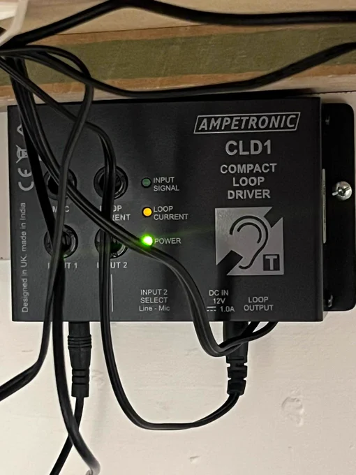 A  close up photograph of a black Ampetronic CLD1 Compact Induction Loop Driver box installed to the underside of a table.