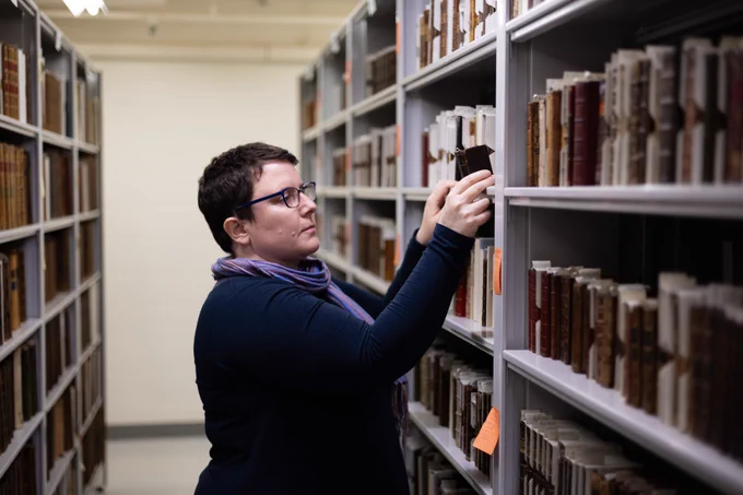 Ruth-Ellen St. Onge with short brown hair and glasses pulls the Officium beatae Mariae virginis off a shelf in the William Ready Division of Archives and Research Collections.