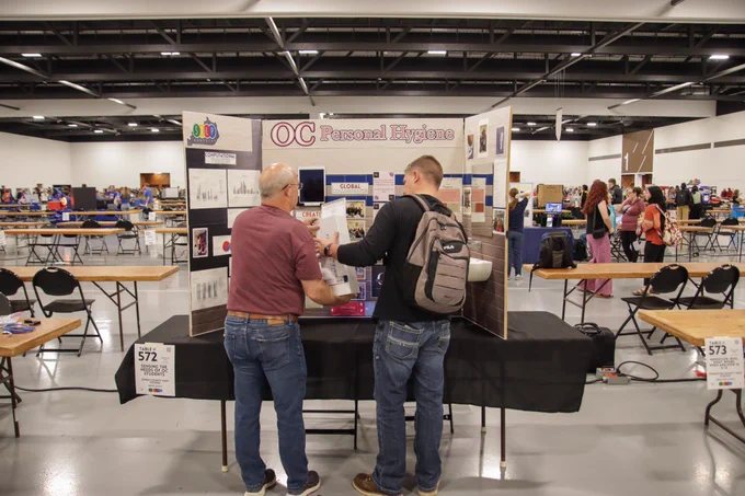 Two people setup a display with “OC Personal Hygiene” displayed at the top
