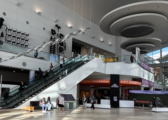 An escalator in the lobby of the convention center with signs pointing up to the higher floor.