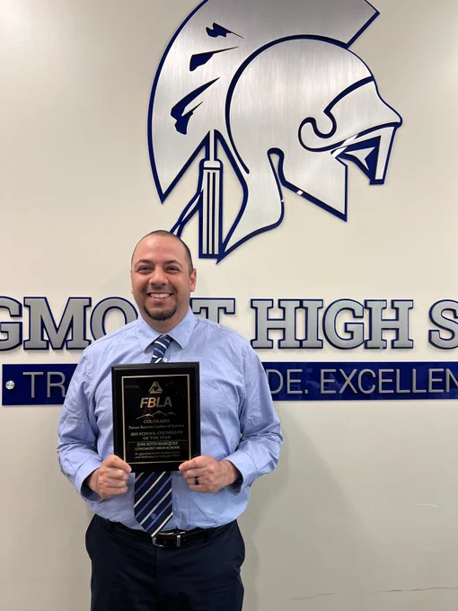 Image of man holding an award in front of a wall