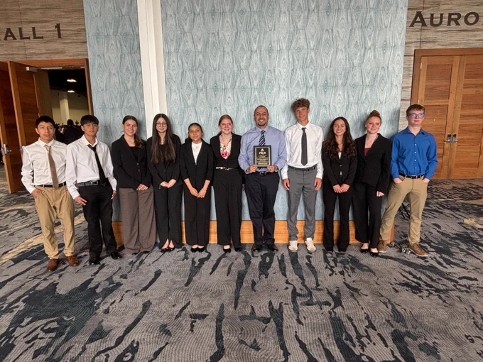 Students in business attire standing with the counselor holding an award