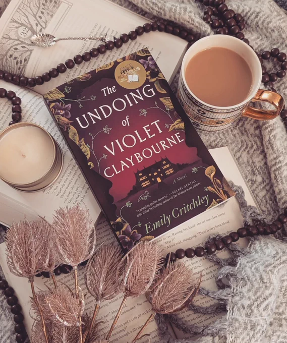 a paperback book surrounded by soft muted colors, more open books, a mug of coffee, a candle