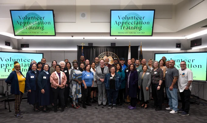 A group of volunteers stands alongside the Chief Probation Officer, posing for a group photo in front of the Probation backdrop. 