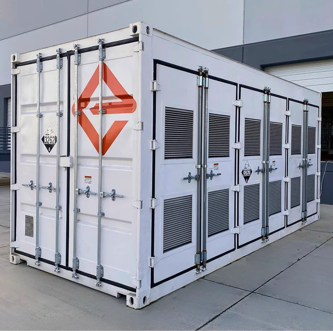 A white shipping-container-like enclosure, filled with batteries and adorned with the logo for Enervenue, sits next to a building
