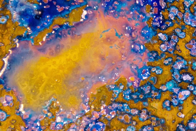 An almost kaleidoscopic composition of metals and minerals, solids and liquids, in bright yellows, purples, and blues.

