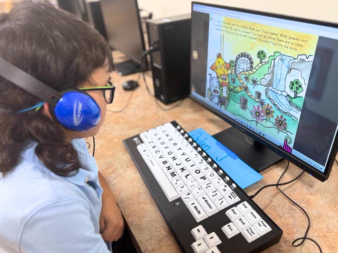 (Photo) A Miami Lighthouse Academy student wears headphones, and is learning computer skills in technology class by playing an educational game on the computer.

