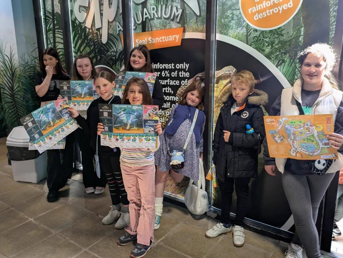 Image shows eight children standing smiling holding maps at the aquarium entrance.