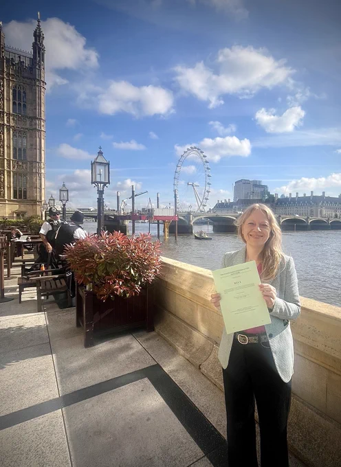 Siân is stood on the terrace of the Houses of Parliament, the River Thames and London Eye are visible in the background, she is smiling holding a copy of her Private Member’s Bill which if passed would ban local and public authorities from using pesticides in public spaces.