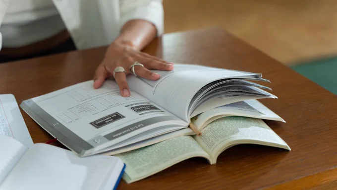 A person studies with open books on a wooden table, focusing on written material.