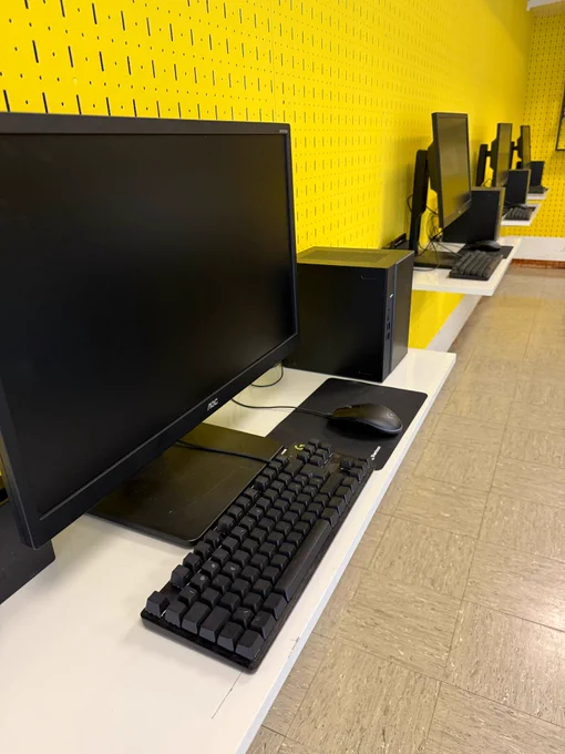 Picture of the four permanent PC/Nintendo Switch setups mounted along a wall in the yellow section of the CastleGames store to be used for regular fighting game and Super Smash Bros. Ultimate events.