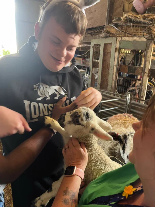 A young man in a black hoodie strokes a black and white lamb. 