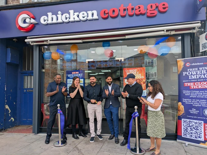 A group of adults clapping after a ribbon has been cut outside of a Chicken Cottage store.