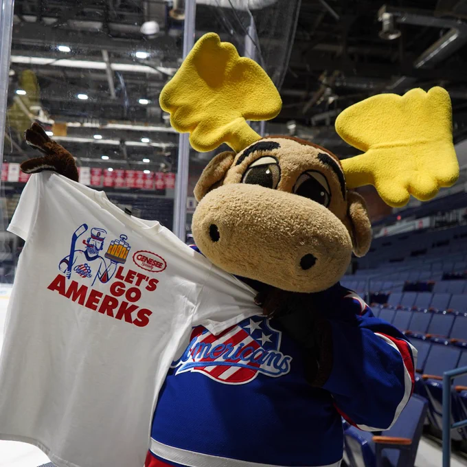 Moose mascot holding up a white Genny T-shirt with red text. 