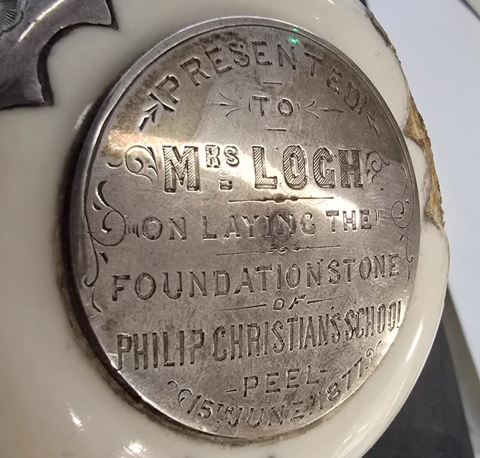 Colour photograph showing in close-up an inscribed silver boss fixed to the head of the mallet. The text reads: 'Presented to Mrs Loch on laying the foundation stone of Philip Christian's School, Peel, 15th June 1877'. 