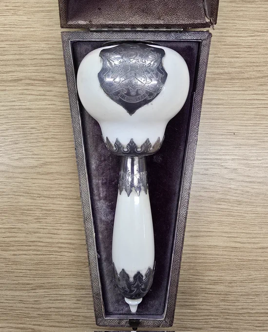 Colour photograph of an ornamental stonemason's mallet in its presentation case. The mallet is made of ivory with silver plaques and decorative trimmings. 