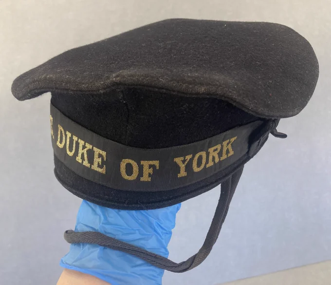 A black felt sailor's cap with 'HMS Duke of York'  written in gold lettering on the cap band.