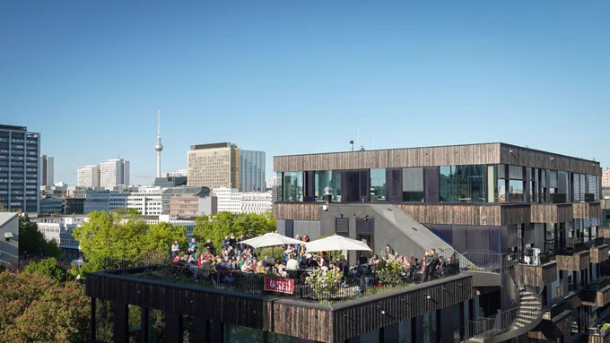 Eine gut gefüllte Dachterrasse. Im Hintergrund die Skyline Berlins mit Fernsehturm.