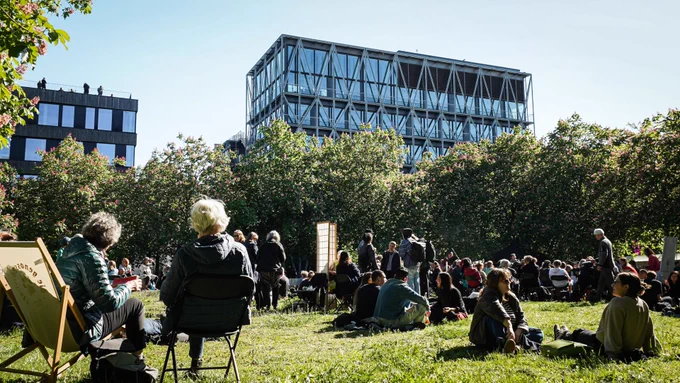 Menschen sitzen auf der Wiese im Besselpark, im Hintergrund das Gebäude der taz.