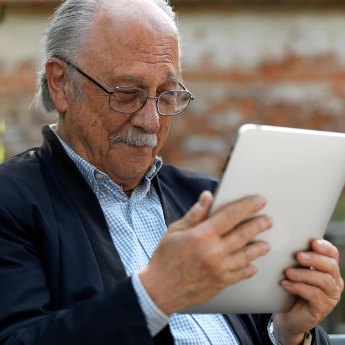 Mature man with glasses using a tablet outside, looking at the screen with a content expression.