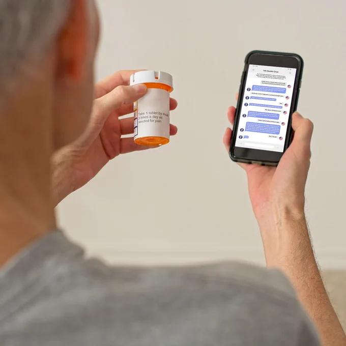 A person holds a prescription bottle in one hand and a smartphone in the other hand, displaying the VA Health Chat app interface.

