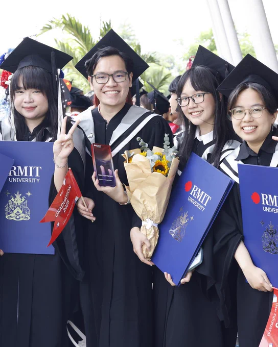 Four RMIT Vietnam graduates in their academic gowns, hold their graduate certificates and smile for the camera