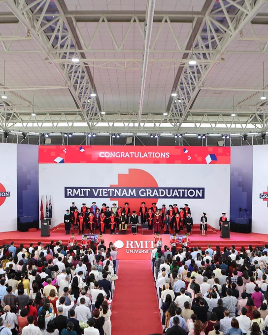 The red-carpeted stage for RMIT Vietnam Graduation, with faculty seated on stage and family and friends seated in front. 
