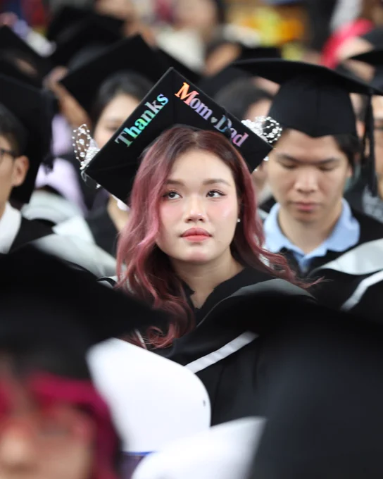 Graduand is looking upwards, her graduate cap is decorated with "Thanks Mom . Dad" 