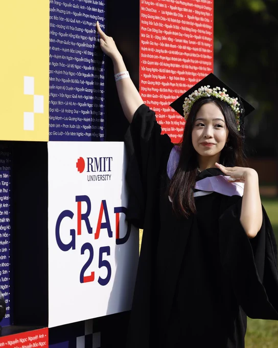 Student points at her name on the board that lists the graduates of 2025, she poses with a smile. 