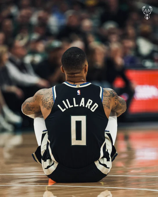 A photo of Damian Lillard sitting on the court at Fiserv Forum.