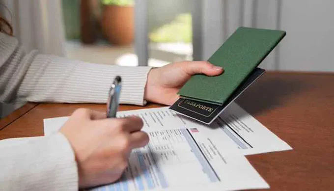 A person filling out immigration forms while holding a green passport, symbolizing the guidance of a Green Card Lawyer.