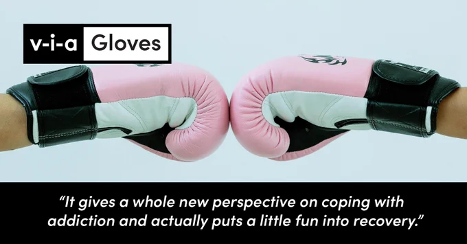 two pink boxing gloves bumping fists against a light blue background, in the upper left corner text reads 'via Gloves' and feedback underneath reads 'It gives a whole new perspective on coping with addiction and actually puts a little fun into recovery', showcasing how boxing can be used as an active and empowering way to manage stress and reframe ways of thinking about substance use.