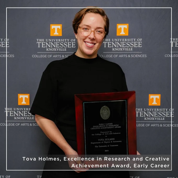 Person holding a commemorative plaque stands in front of a University of Tennessee, Knoxville,  College of Arts and Sciences backdrop. The plaque is from the College of Arts & Sciences and recognizes Tova Holmes as winning an Excellence in Research and Creative Achievement Award for her early career work.