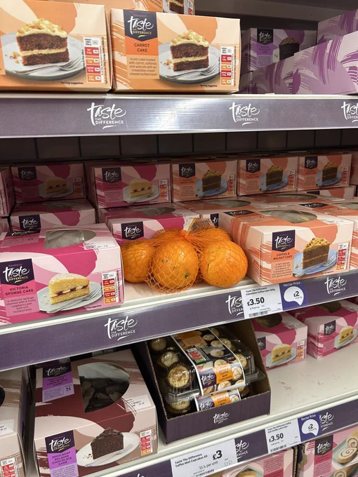 A bag of oranges in the supermarket abandoned on a shelf in the cake aisle, surrounded by cakes