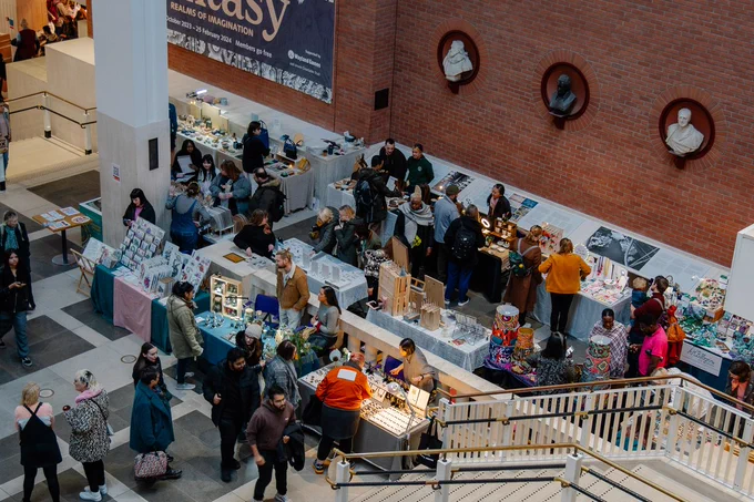 A photo looking over a busy indoor craft market with several stands and sellers selling handmade products.