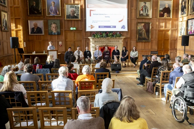 Image shows a panel of speakers being asked a question by a member of the audience at the launch of the Northern Ireland MS Research Hub in the Great Hall at Queen's University.